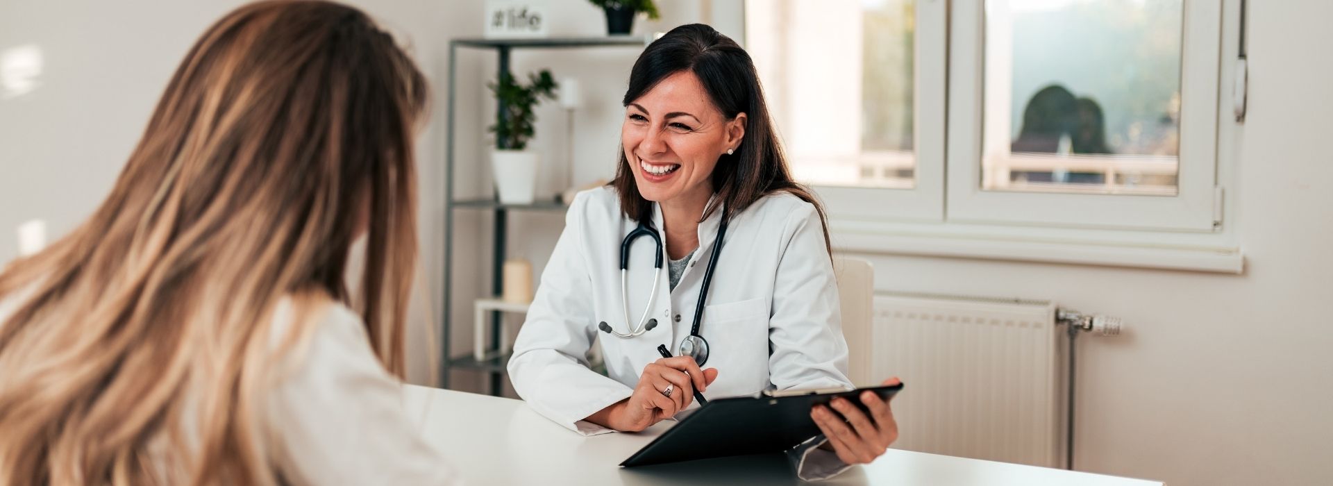 Doctor holding a clipboard talking to a patient at desk